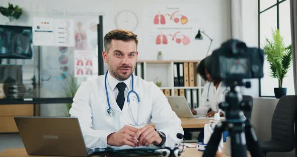 Doctor Sitting in Front of Camera in Own Medical Office and Record Video for His Internet Audience