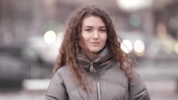 a Young Woman with Curly Hair Poses on a City Street Wearing a Jacket Cold Season