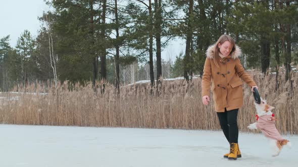 A girl in a coat and yellow boots plays in the winter on the ice of the lake with a dog