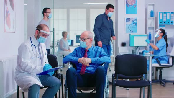 Medical Staff with Face Mask Talking with Disabled Senior Man in Waiting Area