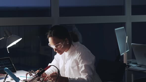 African American Electronics Specialist in Protective Glasses and White Coat Working with Multimeter
