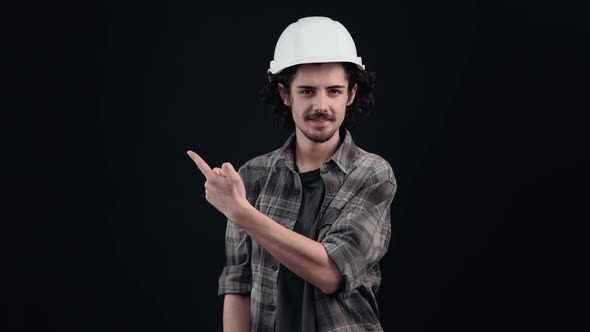 The Charismatic Hipster with the Engineer's White Helmet Looks Cheerful with His Index Finger to One