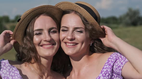 Two Young Twin Girls in Identical Straw Hats and Dresses Looking at the Camera