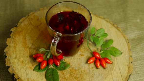 Top View Tincture Of Herbs And Red Berries In A Cup, Tea From Medicinal Rose Hips On A Wooden