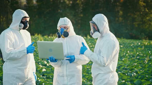 A Group of Agronomists in Protective Suits and Respirators with a Computer