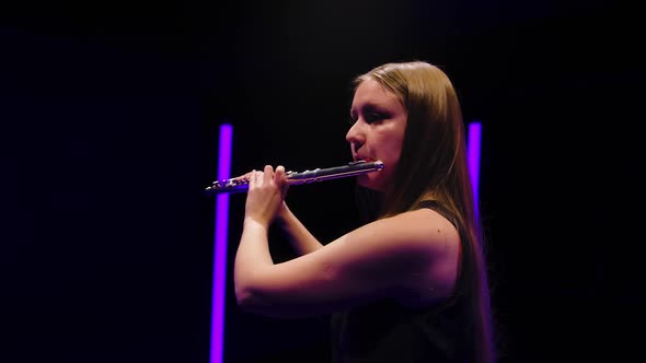 Camera Rotates Around Charming Female Flutist in a Black Dress Against a Background of Bright Neon