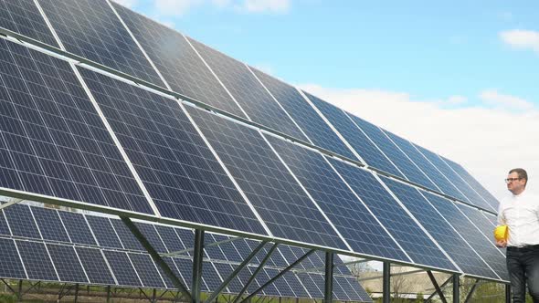 Businessman with Tablet Goes Along the Solar Panels