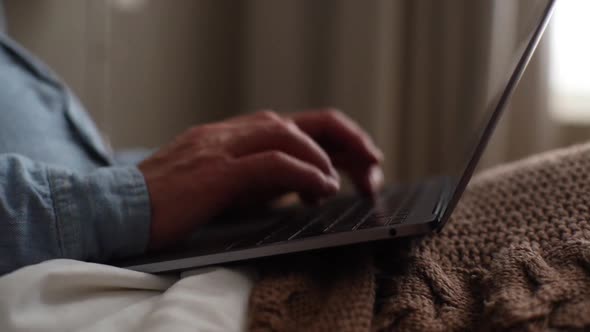 Closeup Hands of Unrecognizable Mature Adult Male Using Typing on Laptop Computer Sitting on Bed