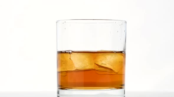 Ice cubes spin in glass of whiskey over white