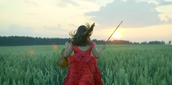 A Girl in a Red Dress with a Violin is Running Across the Field