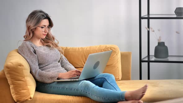 Focused Freelancer Female Working Remotely Use Laptop Relaxing on Yellow Couch