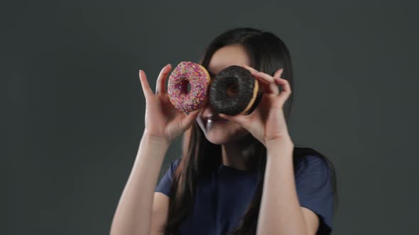 Portrait of Cute Asian Woman Dancing with Sweet Colorful Donuts Isolated on Grey