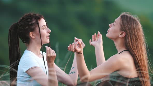 Two Young Women Sitting in Grass and Trying Meditating