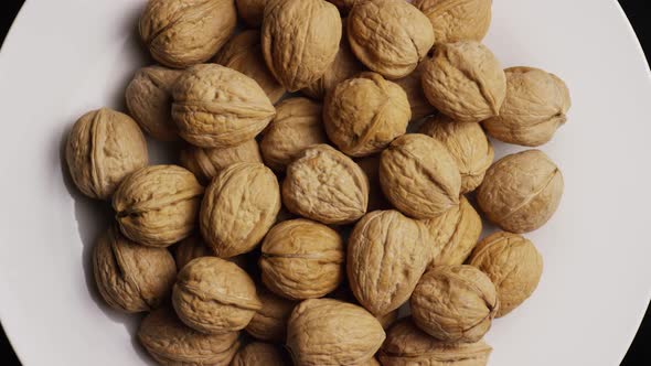 Cinematic, rotating shot of walnuts in their shells on a white surface 