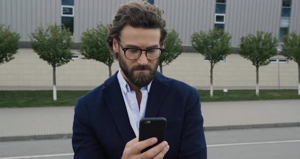 Young Caucasian sexy Scientist in Glasses looking to the Camera and using Phone.