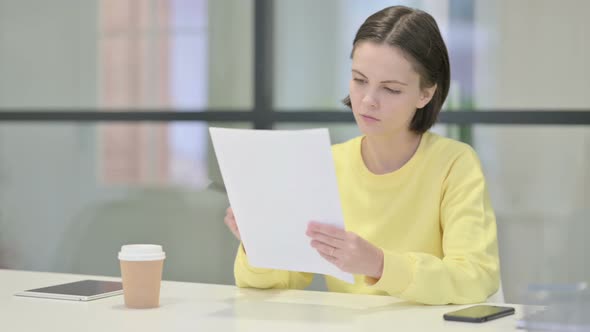 Young Woman Reading Reports While Sitting in Office