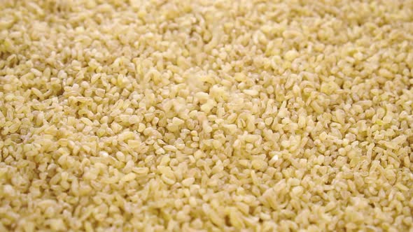 Raw bulgur groats. Falling dry crushed grains in slow motion. Macro