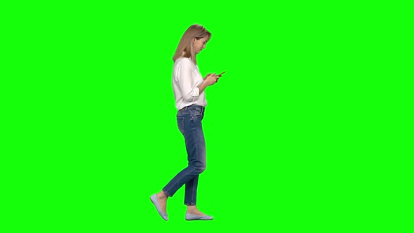 Blonde Woman Is Calmly Walking and Texting Message Vie Her Mobile Phone on Green Screen. Profile