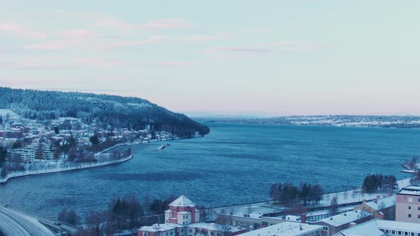 Wide aerial rise from city of Östersund towards waters on winter day