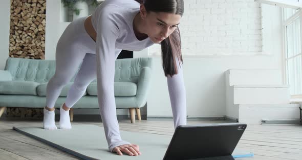 Brunette with Long Ponytail Looks at Tablet Display and Practices Exercise