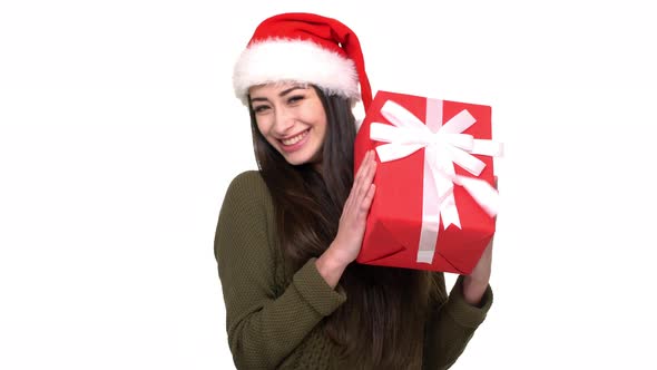 Portrait of Young Woman in Santa Claus Red Hat Shaking Gift Box Being Happy Giving Amazing New Year