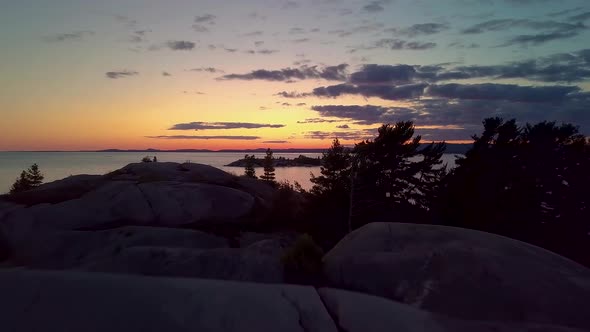 Fly Past Inukshuk on Rocky Pine Tree Island just after Sunset, Drone Aerial Wide Dolly In. Colorful