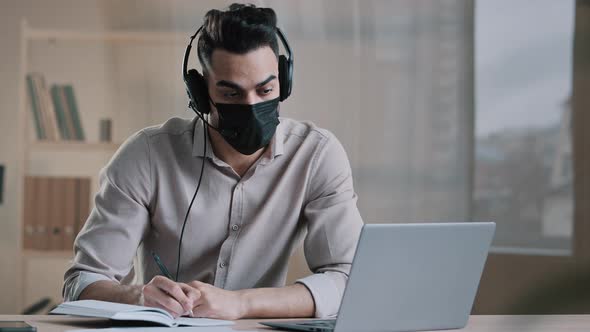 Young Arab Man Freelancer Male Writer in Medical Mask Wear Headphones Sit Home Office During