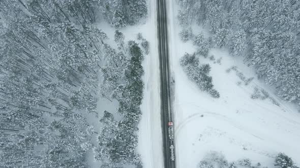 Car Driving on Snow Road Through Winter Forest Aerial View