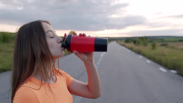 Portrait of Girl Drinking From Sport Flask and Looking Into Camera Outdoors