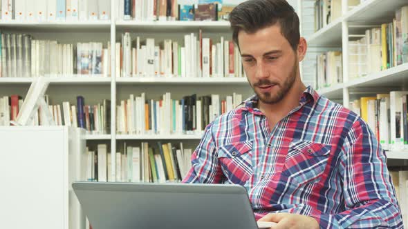 Cheerful Guy Looks at Laptop and Laughs