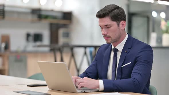 Serious Businessman with Laptop Looking at Camera in Office