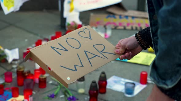 Placing an antiwar sign between candles and Ukraine flags on pavement.