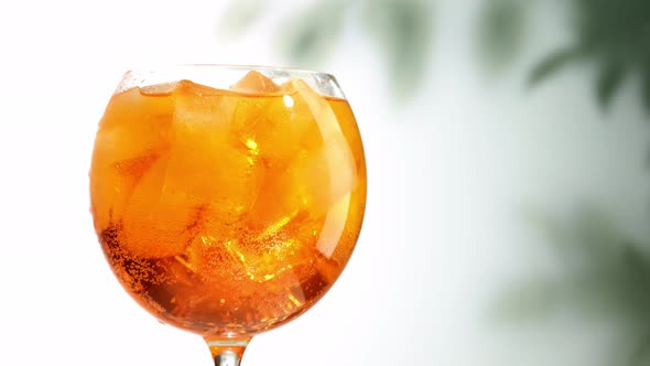 glass of aperol spritz cocktail with ice turning on defocused leaves background zoom in