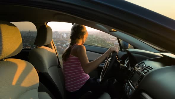 Young woman standing near her car enjoying warm sunset view. Girl traveler leaning on vehicle 