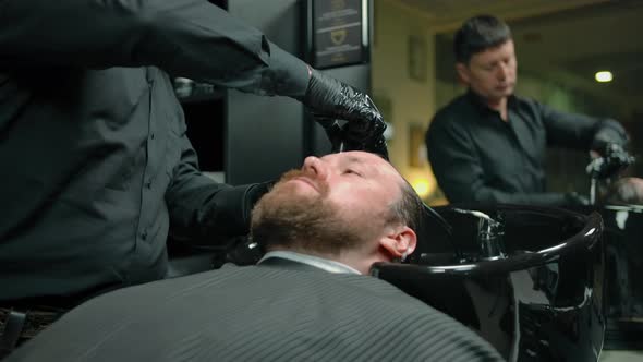 Bearded Man Washed with Shampoo Foam in a Barbershop By Professional Barber
