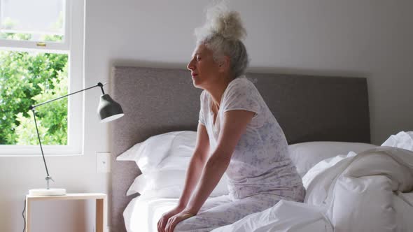 Sleepy senior caucasian woman sitting on the bed at home