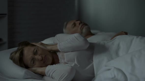 Man Snoring in Bed, Woman Beside Him Pressing Hands Against Ears, Troubled Sleep