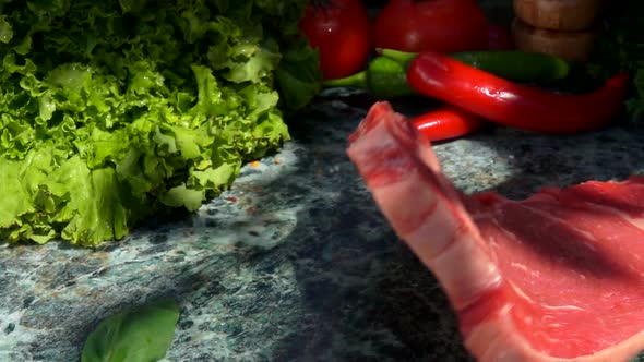 Raw Steak is Falling on a Stone Table on the Background of Vegetables Outdoors