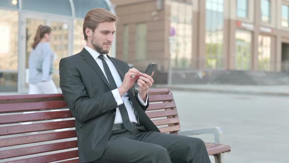 Businessman Celebrating Online Success on Smartphone While Sitting Outdoor on Bench