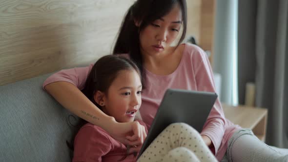 Positive Asian mother and daughter looking at the tablet