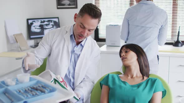 Caucasian male dentist with dental nurse examining teeth of female patient at modern dental clinic