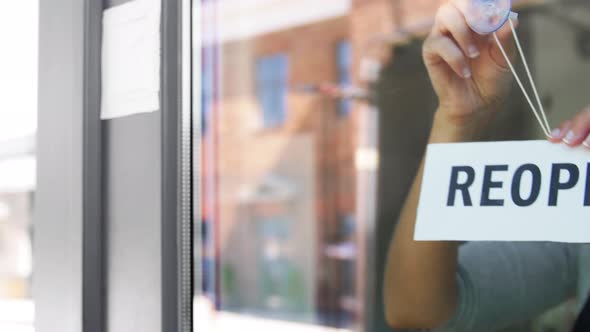 Happy Woman Hanging Reopen Banner to Door Glass