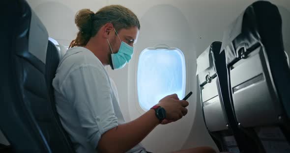 Man in a Medical Mask Texting During the Flight