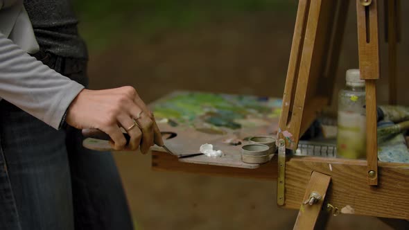 A Girl's Hand Smearing a White Oil Paint with a Spatula Over the Palette