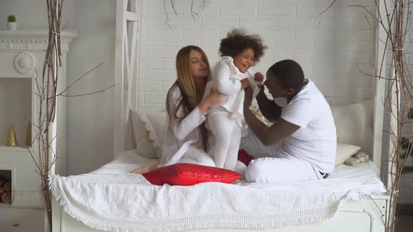 Young Happy Multi-ethnic Family of Mother, Father and Little Daughter Dressed in White at Background