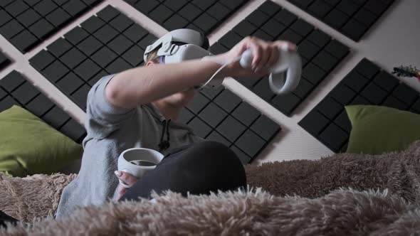 Young Woman Sitting on Sofa Playing Game Using VR Helmet Indoor at Home