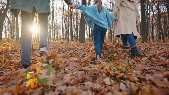 Unknown Parents Walking By Yellow Foliage in Autumn Park Holding Hands of Little Daughter