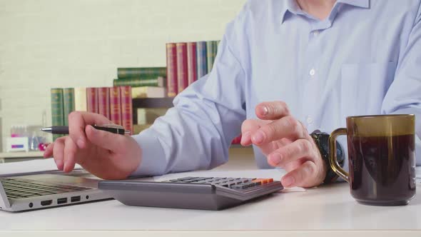 A Man Working in the Office Works with Calculator and Laptop