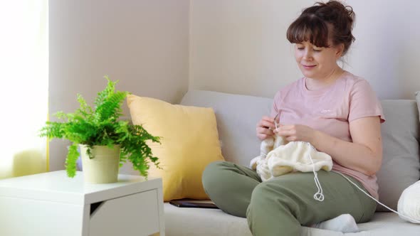 Young Woman Knitting White Knitwear on Sofa at Home