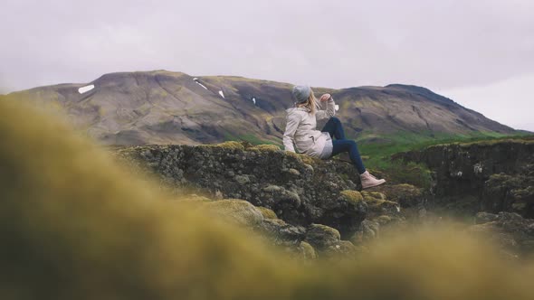 Happy Young Hipster Woman Sits on Rock with Mountains Background and Enjoying Nature Slow Motion